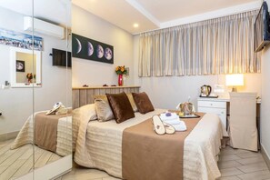 A hotel room with two beds, a desk, a chair, a TV, a painting of moons, and a window with curtains. - Capodichino International Hotel (Naples)