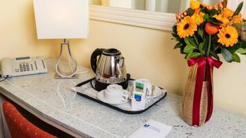 Ein Hotelzimmer-Tresen mit einer Kaffeemaschine, einem Telefon und einem Tablett mit Tassen und einer Taschentuchbox. Eine Vase mit Blumen steht rechts.