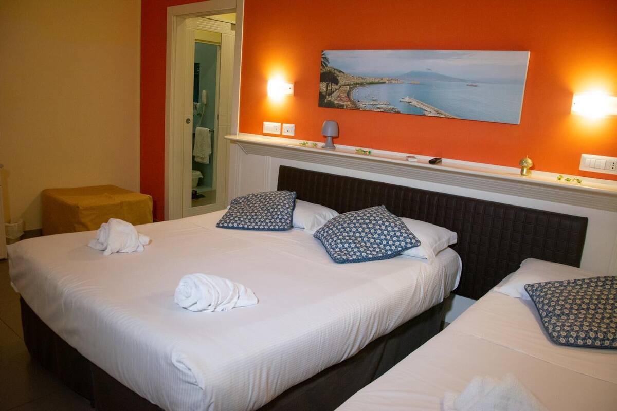 A hotel room with two beds, a painting of a coastal scene, and a small table with a lamp.