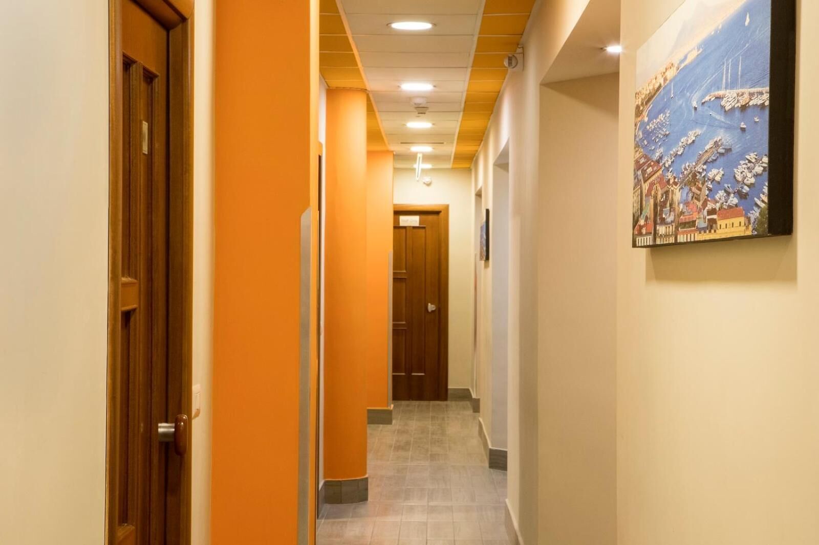 A hotel corridor with orange walls, wooden doors, and a tiled floor.