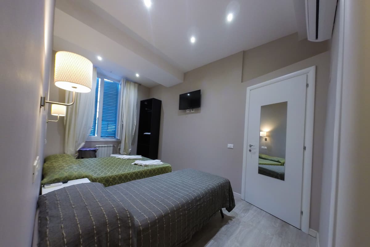 Camera d'albergo con due letti, una TV, un armadio e una porta con uno specchio.