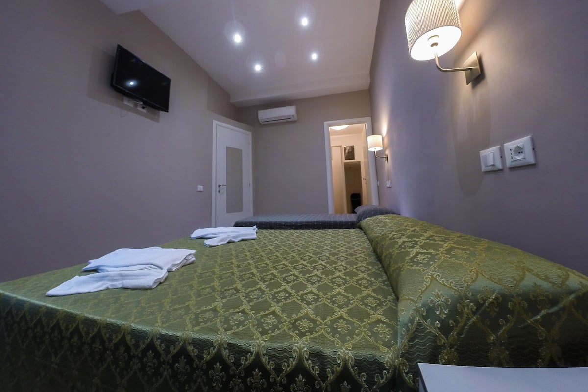 Una camera d'albergo con un letto, una TV fissata al muro e una lampada a parete.