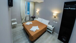 A hotel room with a bed, a chair, a desk, a TV, and a window with curtains. - Casa Barberini (Rome)