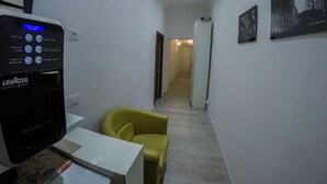A narrow hallway with a coffee machine, a yellow chair, and framed pictures on the wall. - Casa Barberini (Rome)