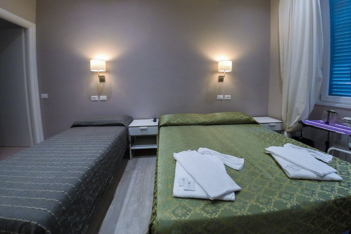 Camera d'albergo con due letti, un tavolino e due lampade a parete.