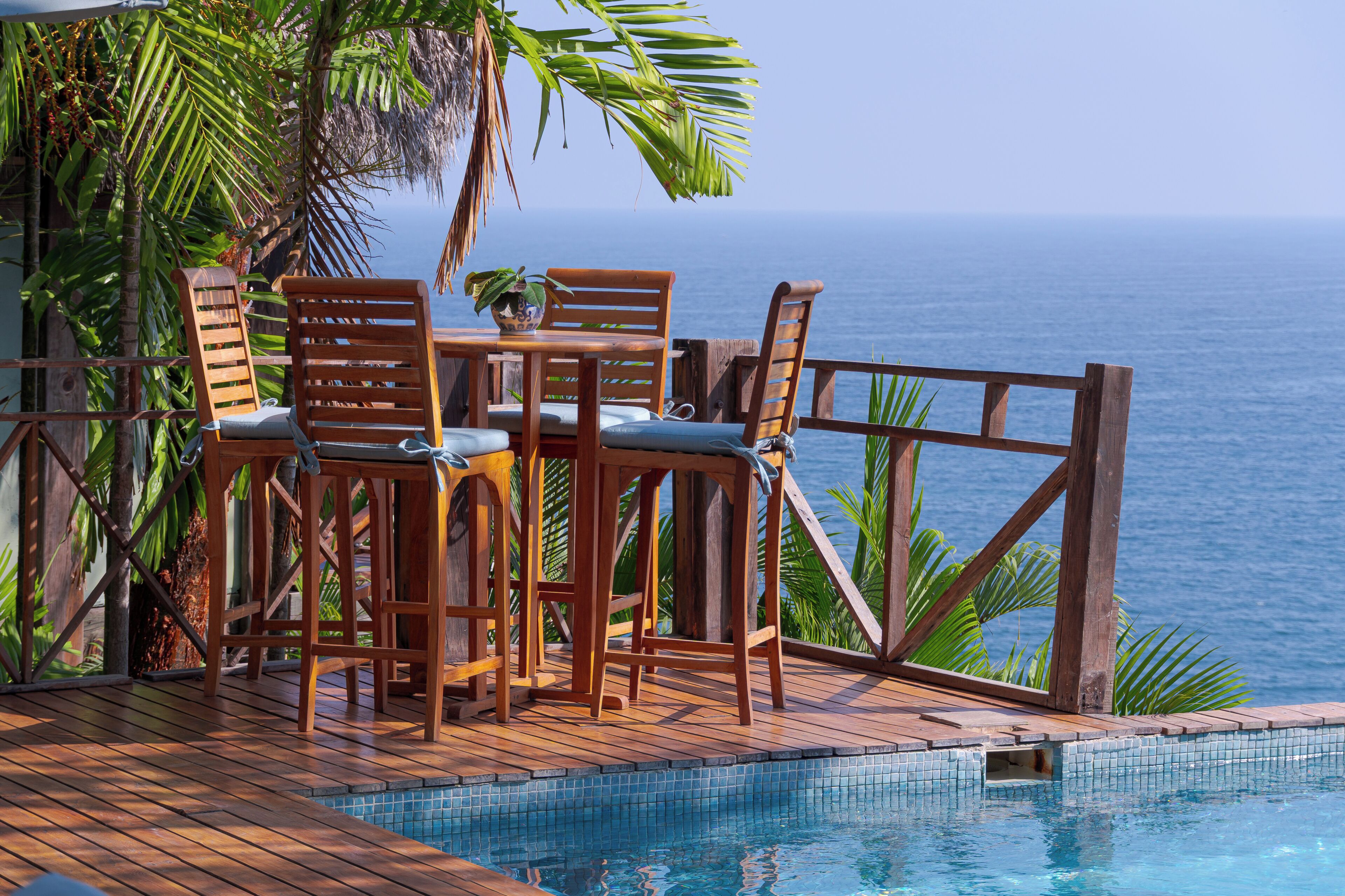 A wooden deck with a pool, chairs, and a table overlooking the ocean.