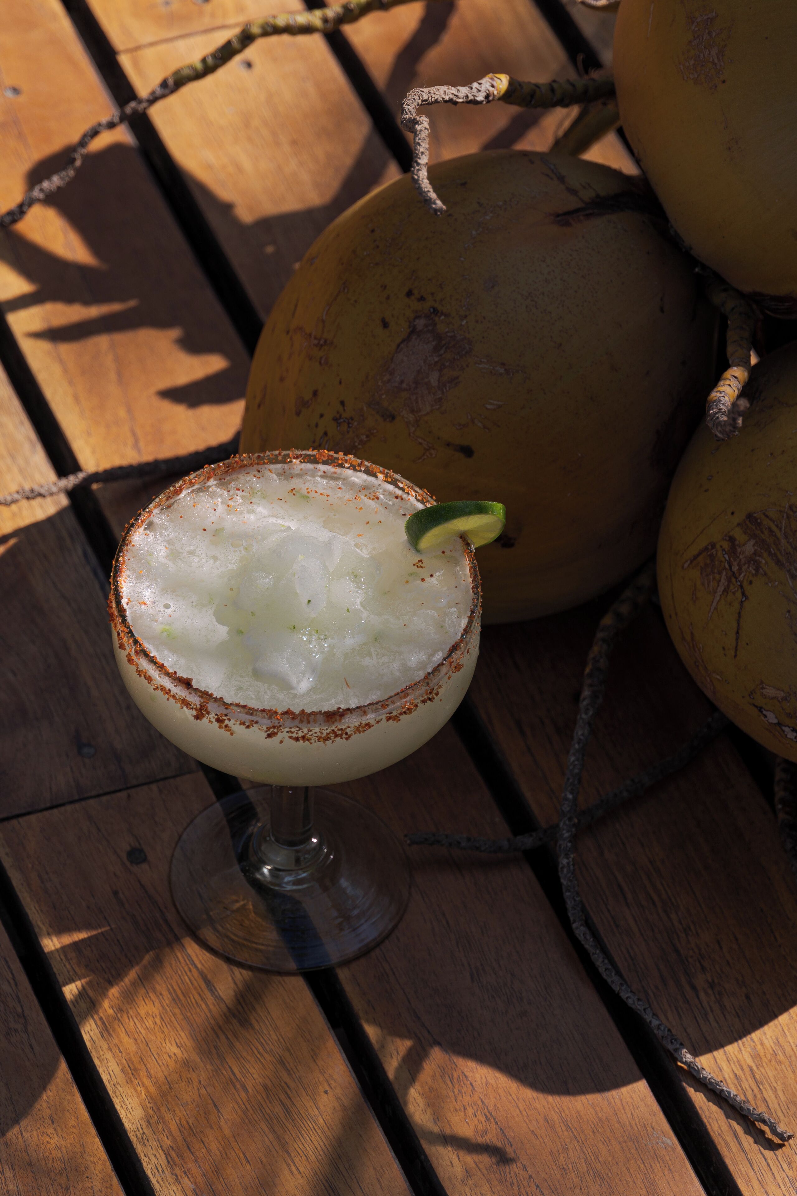 A cocktail in a glass with a lime garnish, placed on a wooden table with a metal grid.