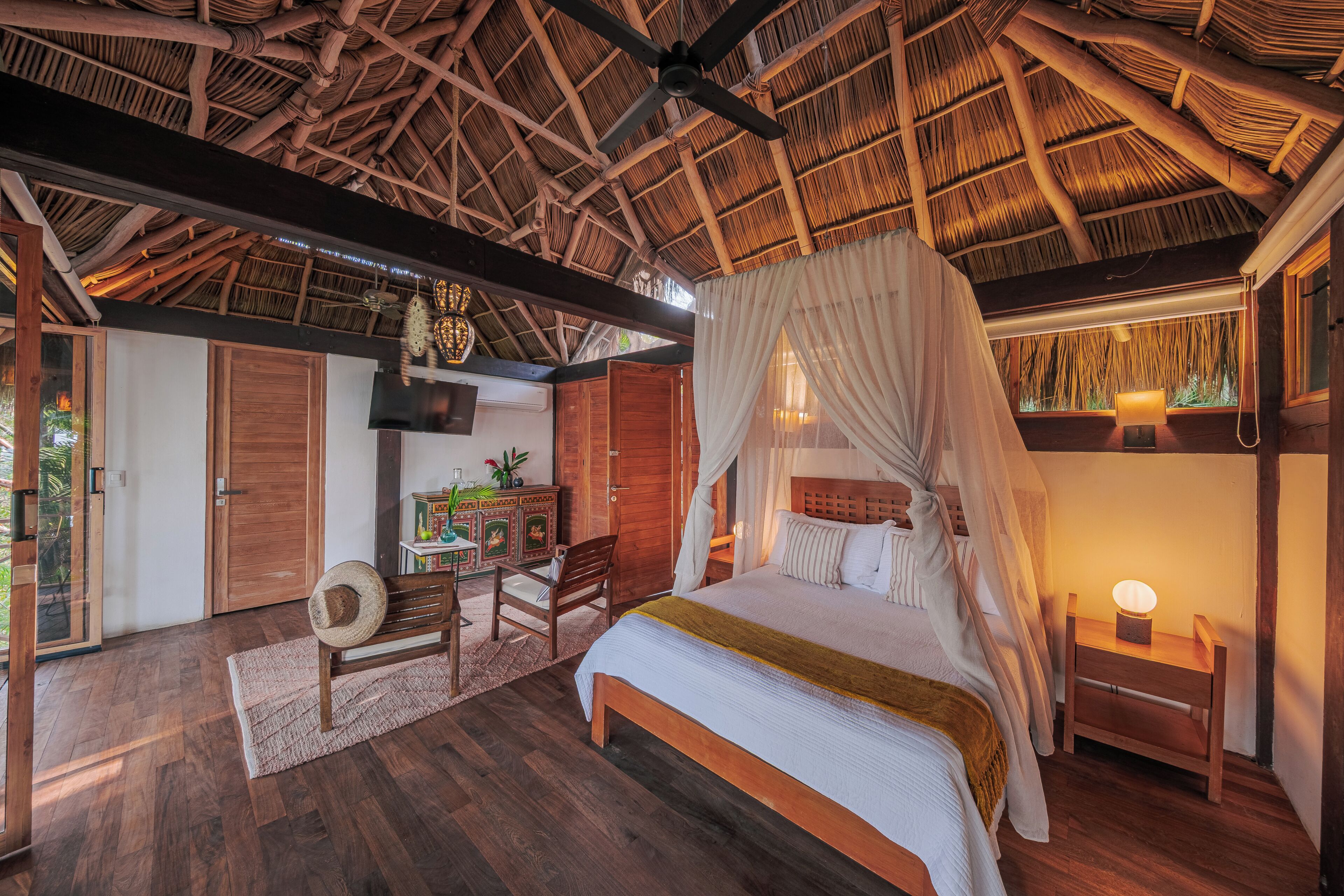 A room with a bed, a chair, a desk, a small table with a lamp, and a ceiling fan.