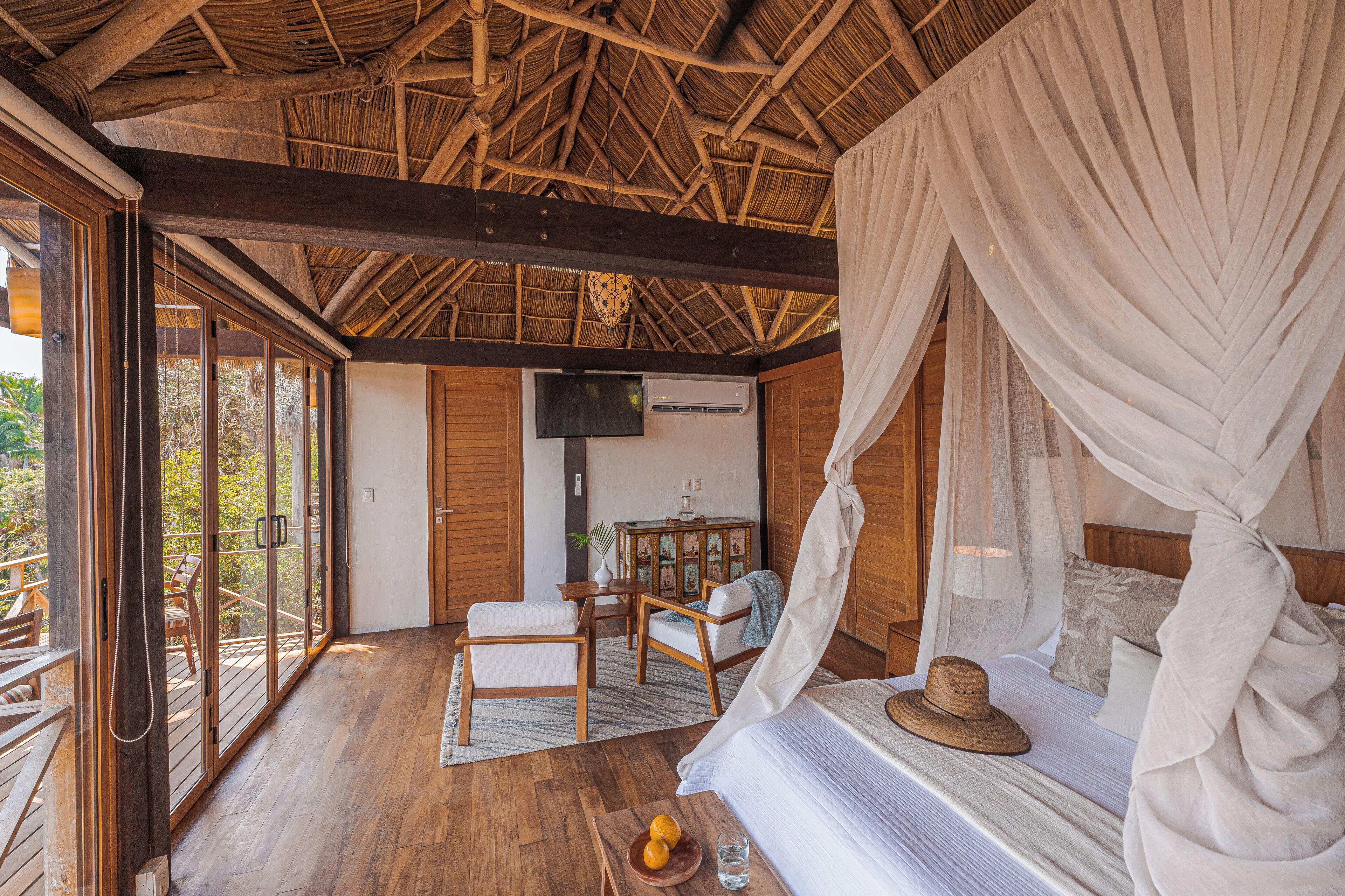 A room with a bed, a TV, a wooden floor, and a large window.