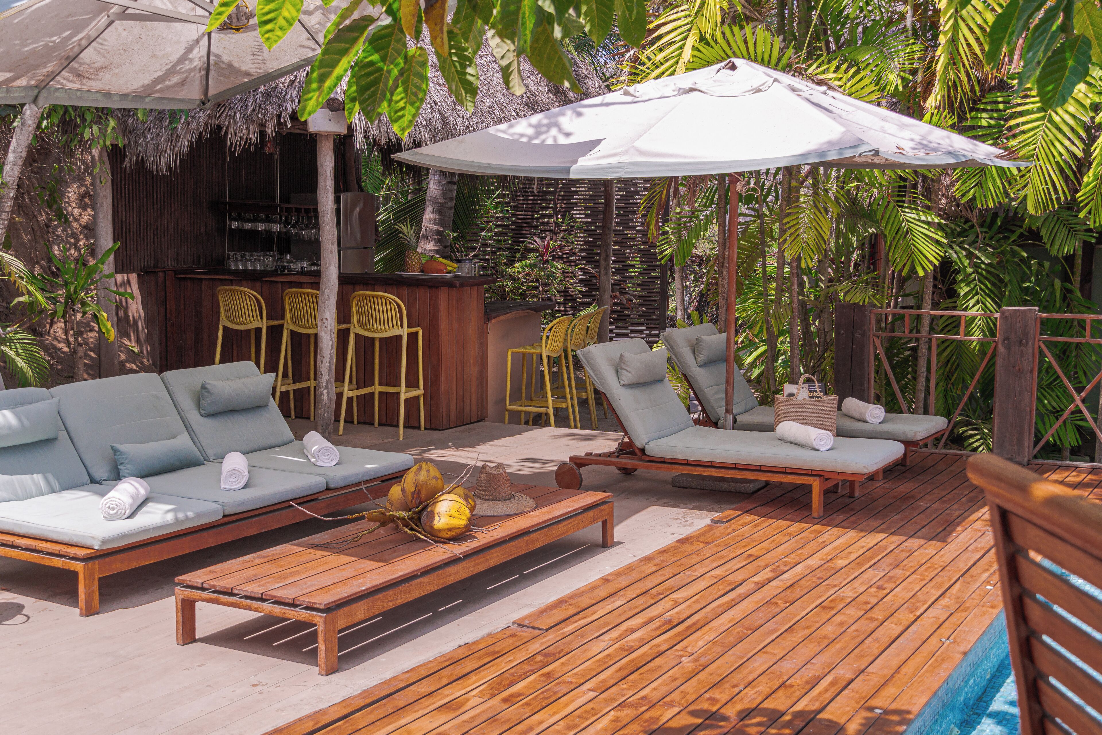 A wooden deck with lounge chairs and a sofa, a bar area, and a pool.