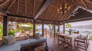 Una terraza al aire libre con mobiliario de madera, techo de paja y vista al mar.