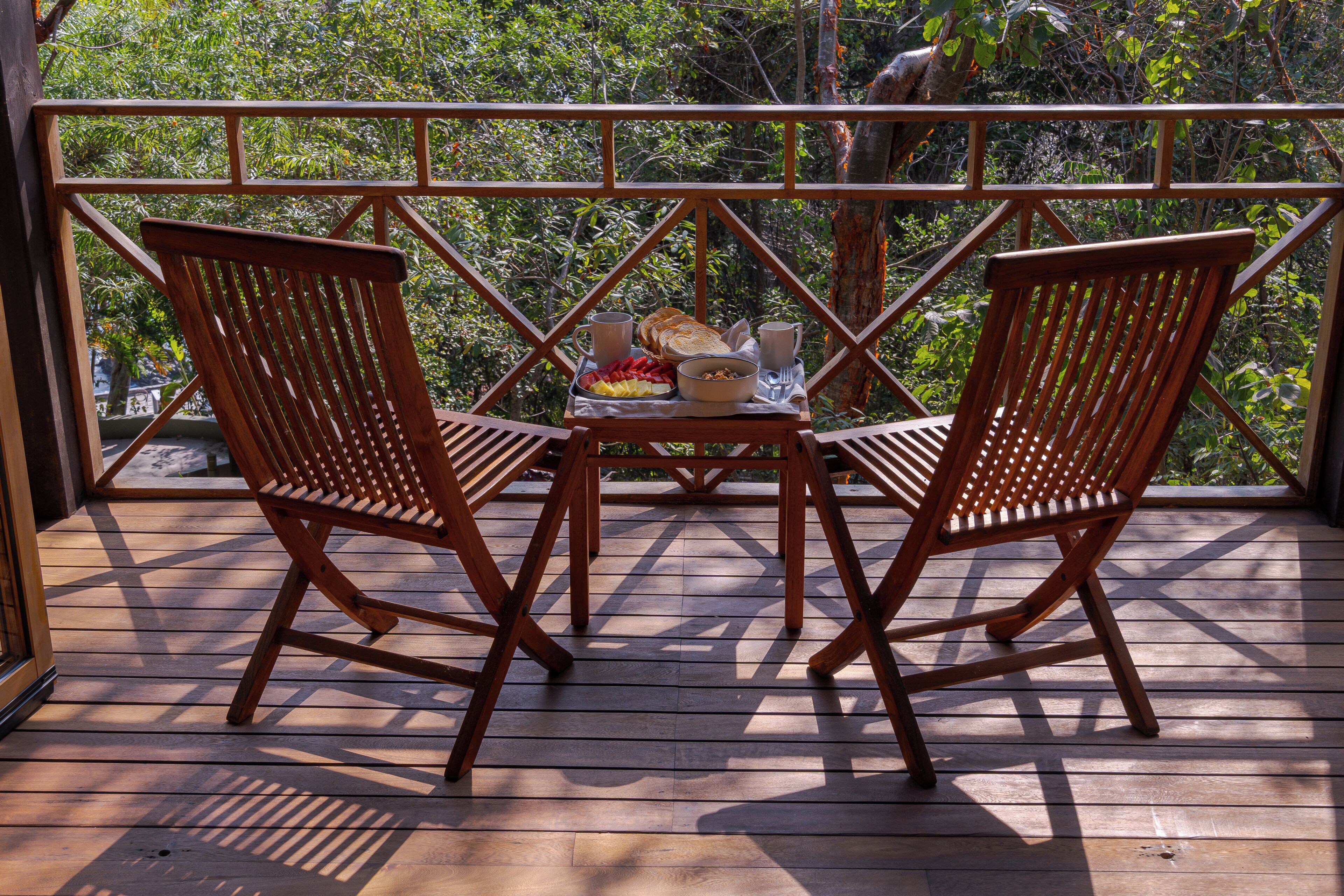 A wooden deck with two wooden chairs and a table set for breakfast.