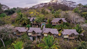 Un resort con cabañas de techo de paja, piscina y exuberante vegetación tropical.
