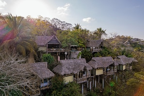 A series of thatched-roof cottages with balconies, surrounded by lush vegetation and a clear sky.