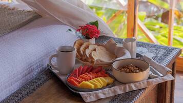 A tray with sliced fruits, bread, coffee, and a bowl of cereal on a table with a view of greenery.