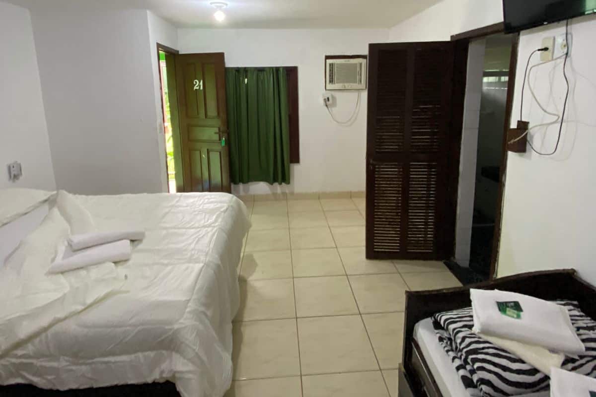 A hotel room with a bed, a sofa, a television, and an air conditioning unit.