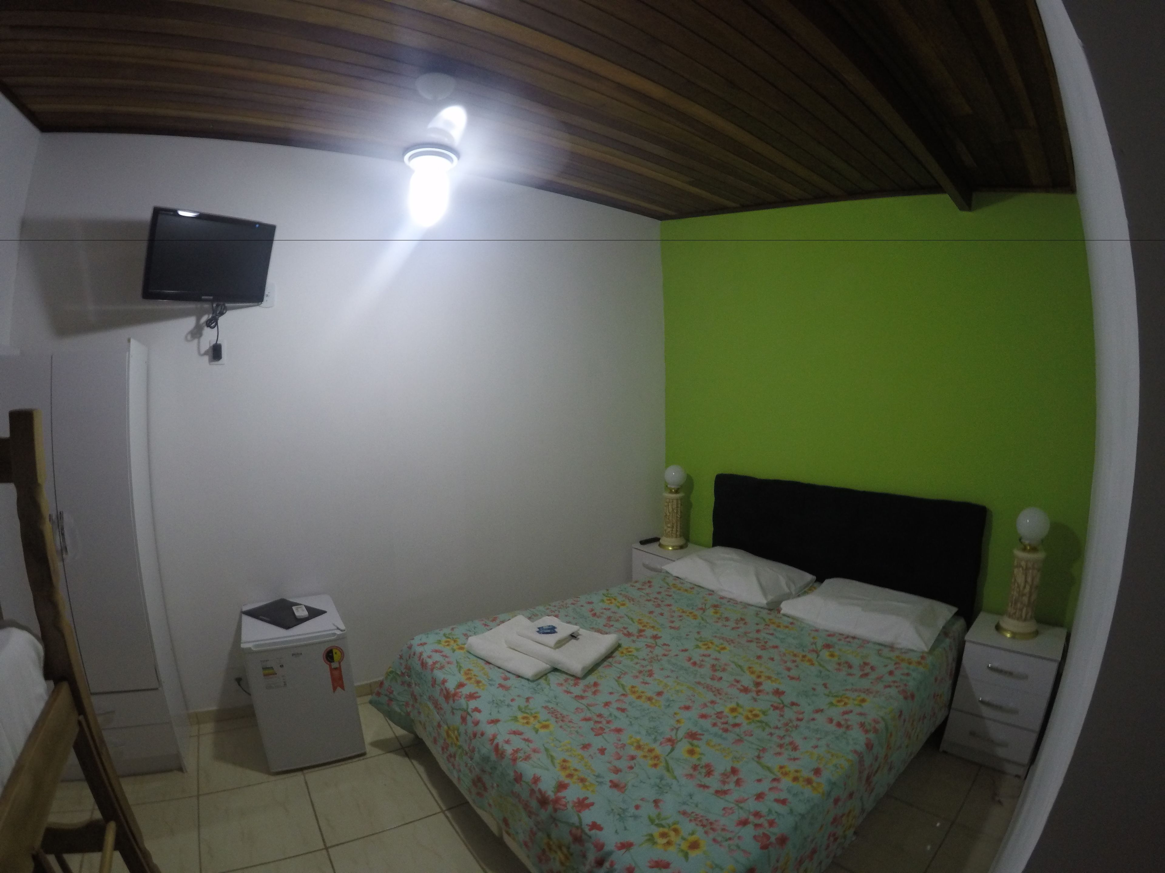 Un dormitorio con una cama, un televisor montado en la pared, un refrigerador pequeño y una pared de acento verde.
