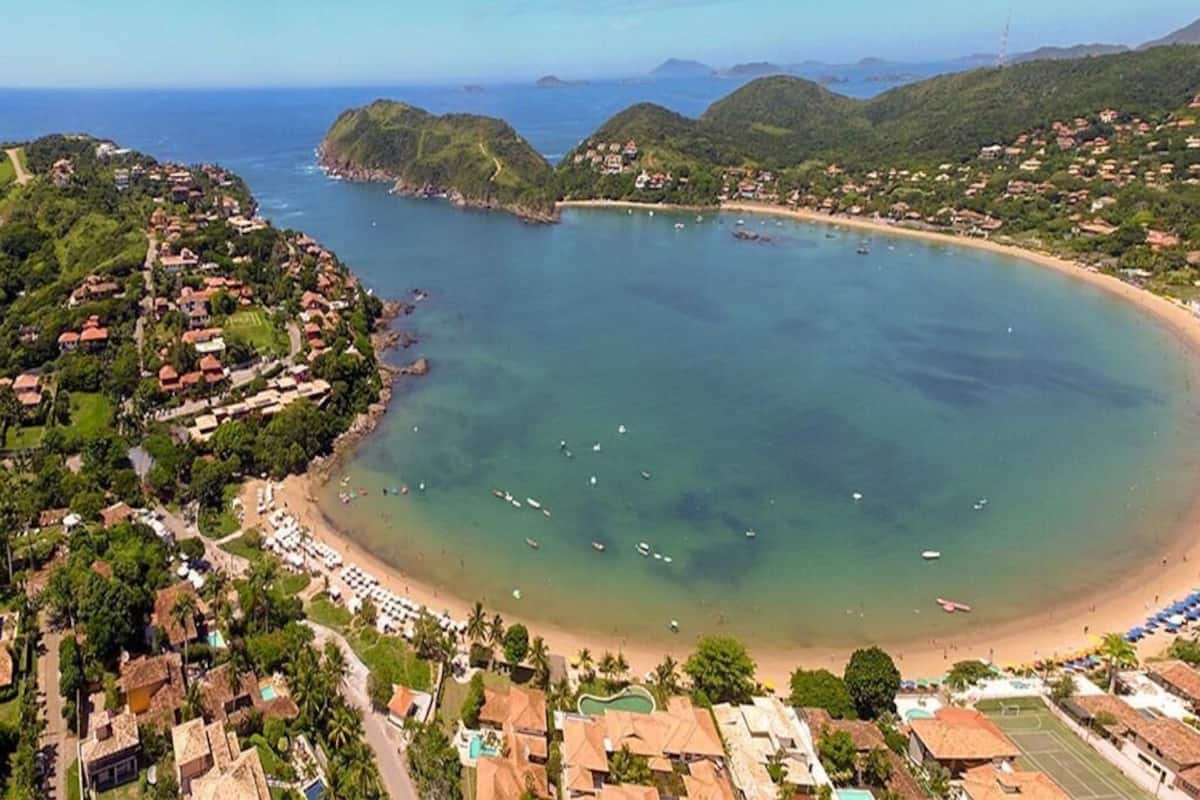 An aerial view of a coastal town with a beach, clear waters, and surrounding hills.