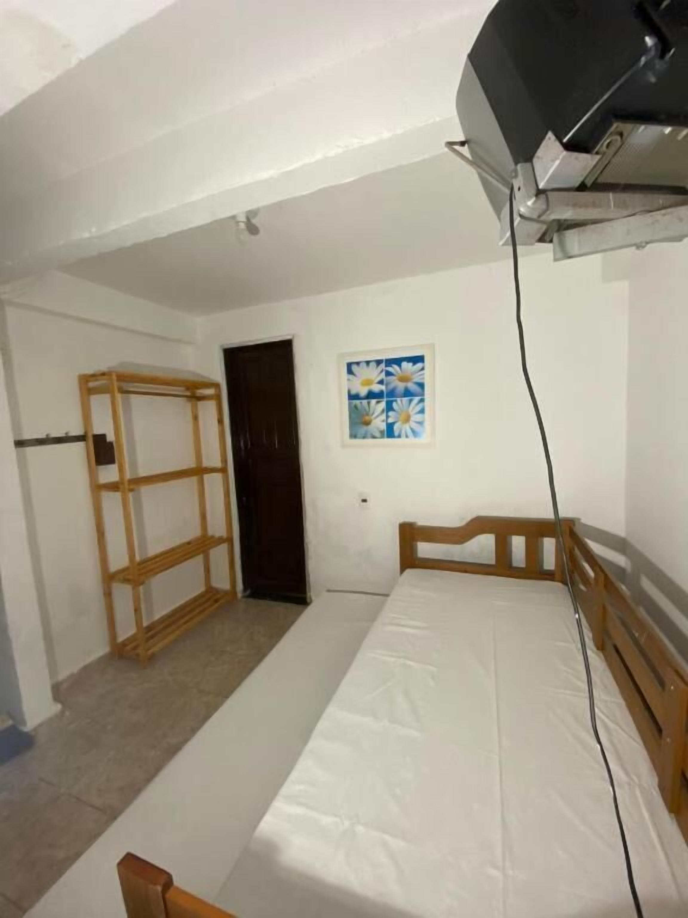 A bedroom with a wooden bed frame, a white mattress, a wooden wardrobe, and a painting of daisies on the wall.
