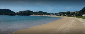 A beach with a sandy shore, calm water, and a hilly background with buildings. - Pousada Ferradura Beach (Búzios)
