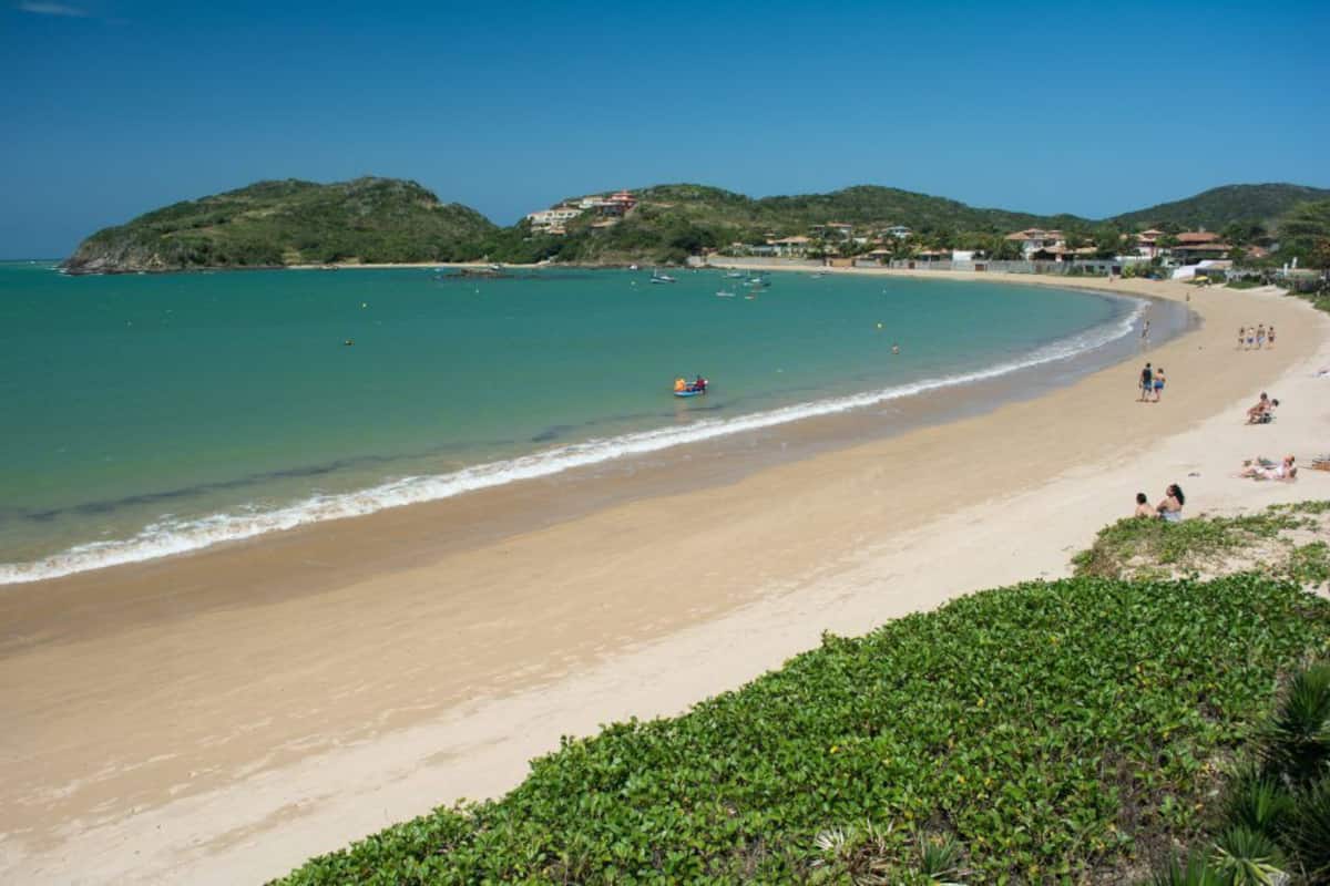 A beach with clear turquoise water, a sandy shore, and hills in the background.