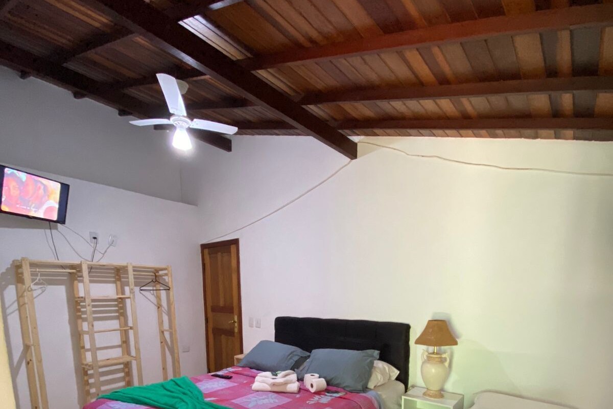 Un dormitorio con dos camas, ventilador de techo, televisor y escalera de madera.