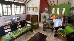 Una habitación amplia con techo alto, una zona de comedor con mesa y sillas, y un área de juegos con una casita y juguetes.