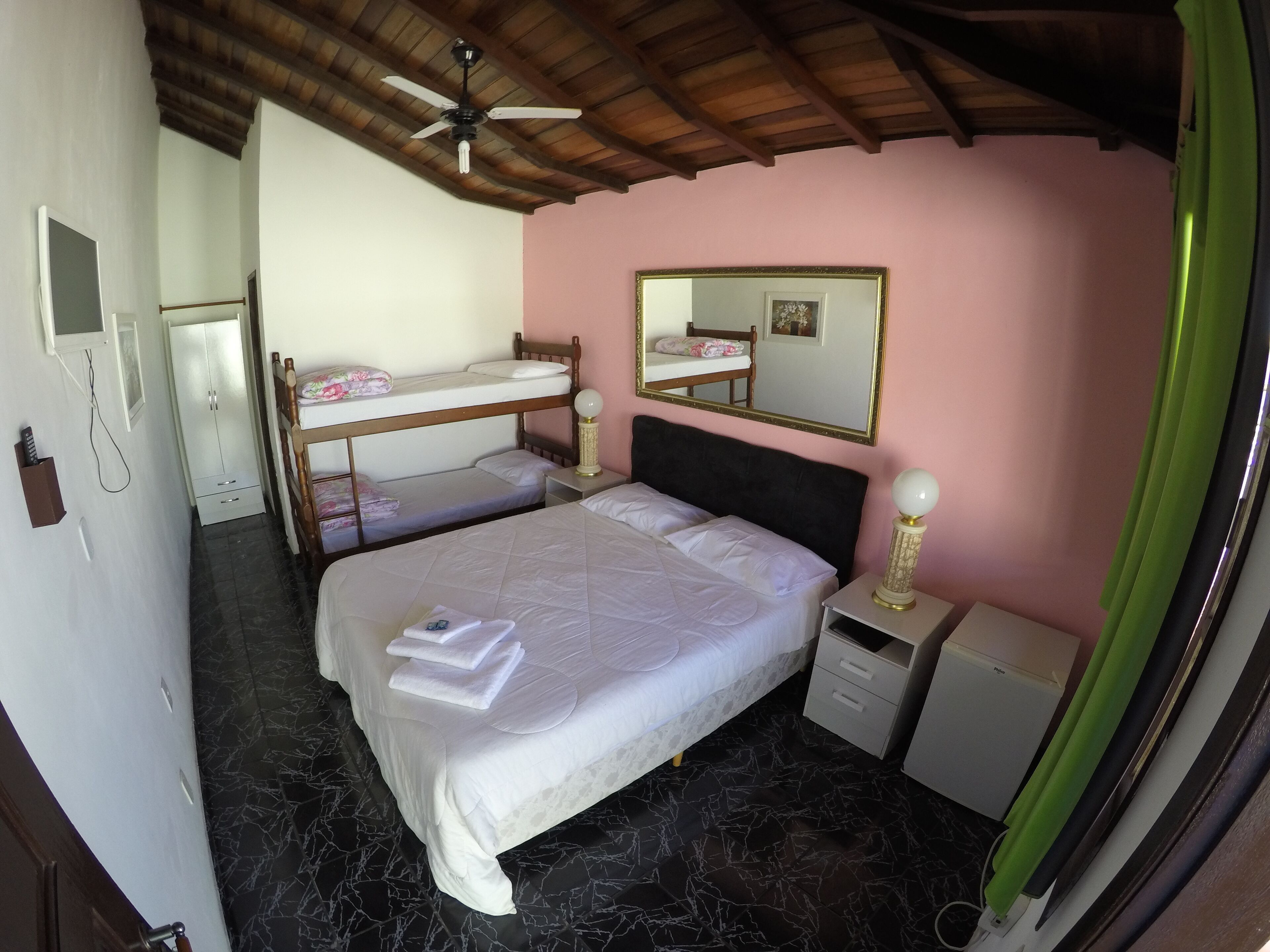 A bedroom with a bunk bed, a single bed, a mirror, a bedside table, and a ceiling fan.