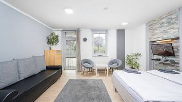 A modern bedroom with a bed, a sofa, a small table, two chairs, a TV, and a window with curtains.