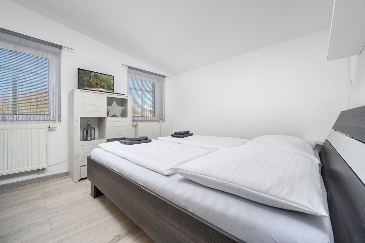 Quarto moderno com cama grande, mesa de cabeceira, radiador e janela com persianas.