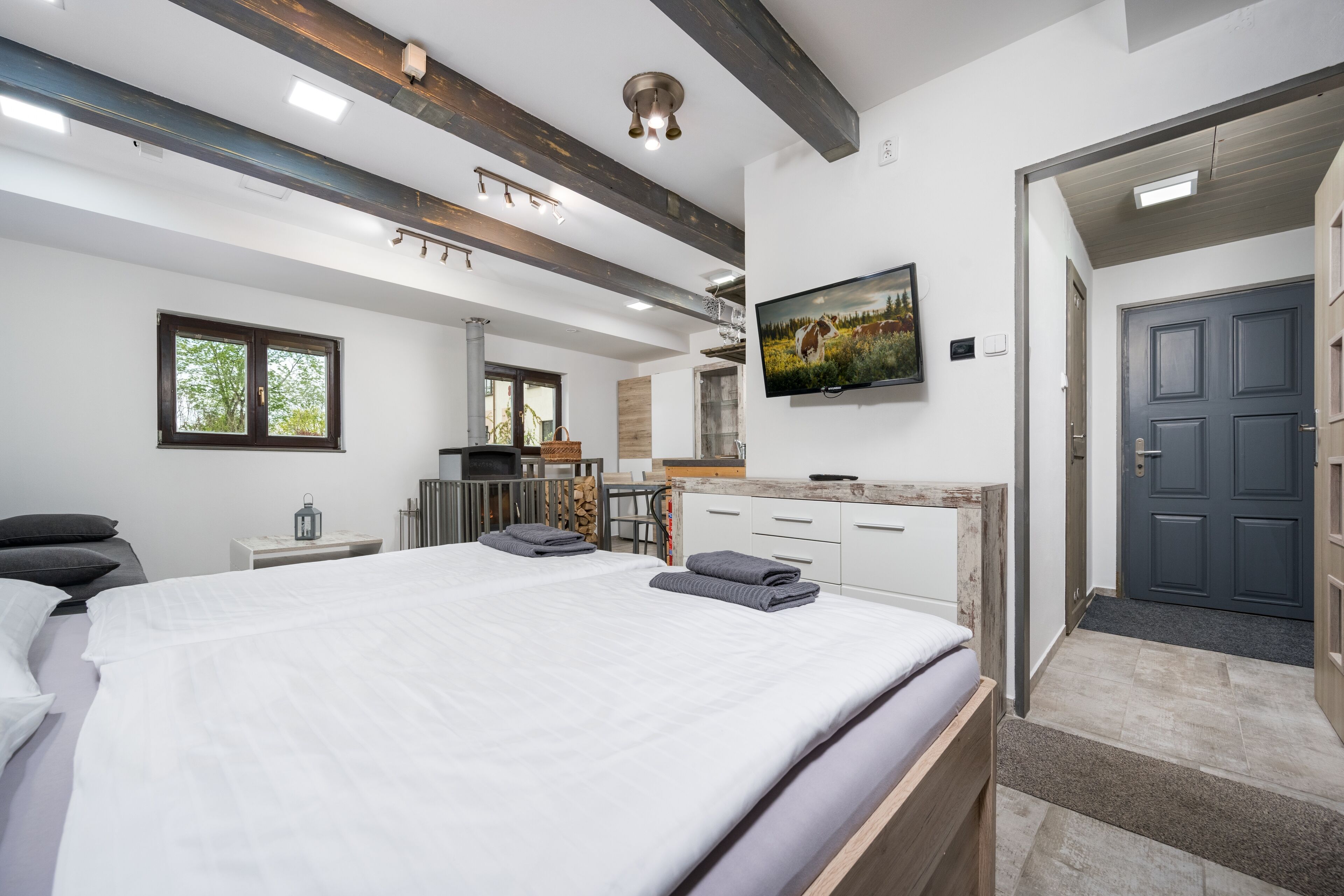 Un dormitorio moderno con una cama grande, un televisor en la pared y techo de madera.