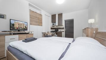 Ein modernes Hotelzimmer mit einem großen Bett, einem Schreibtisch mit Computer, einer Mikrowelle und einem Fernseher, der ein Gebäude zeigt.