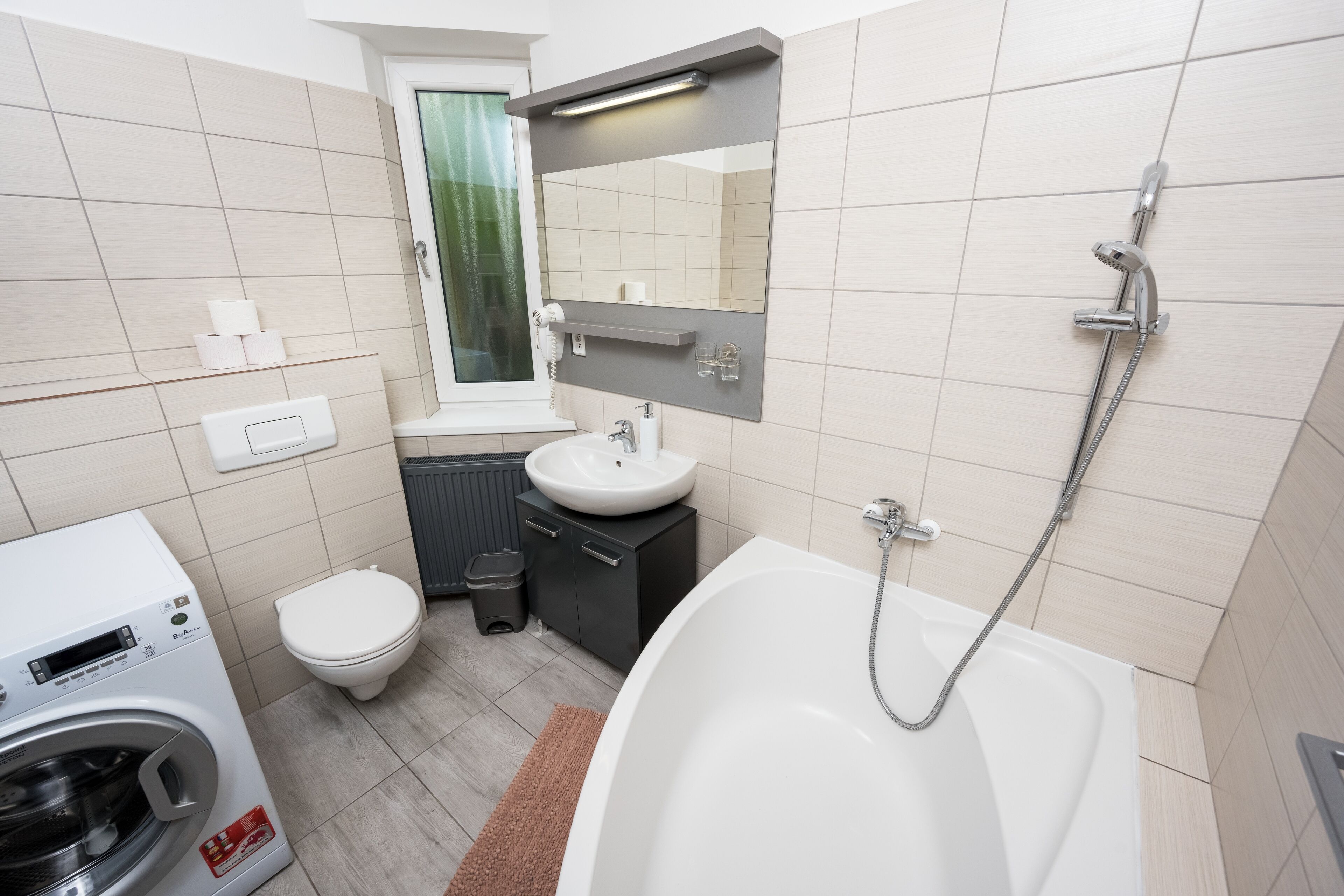 A modern bathroom with a white bathtub, a toilet, a sink, and a washing machine.