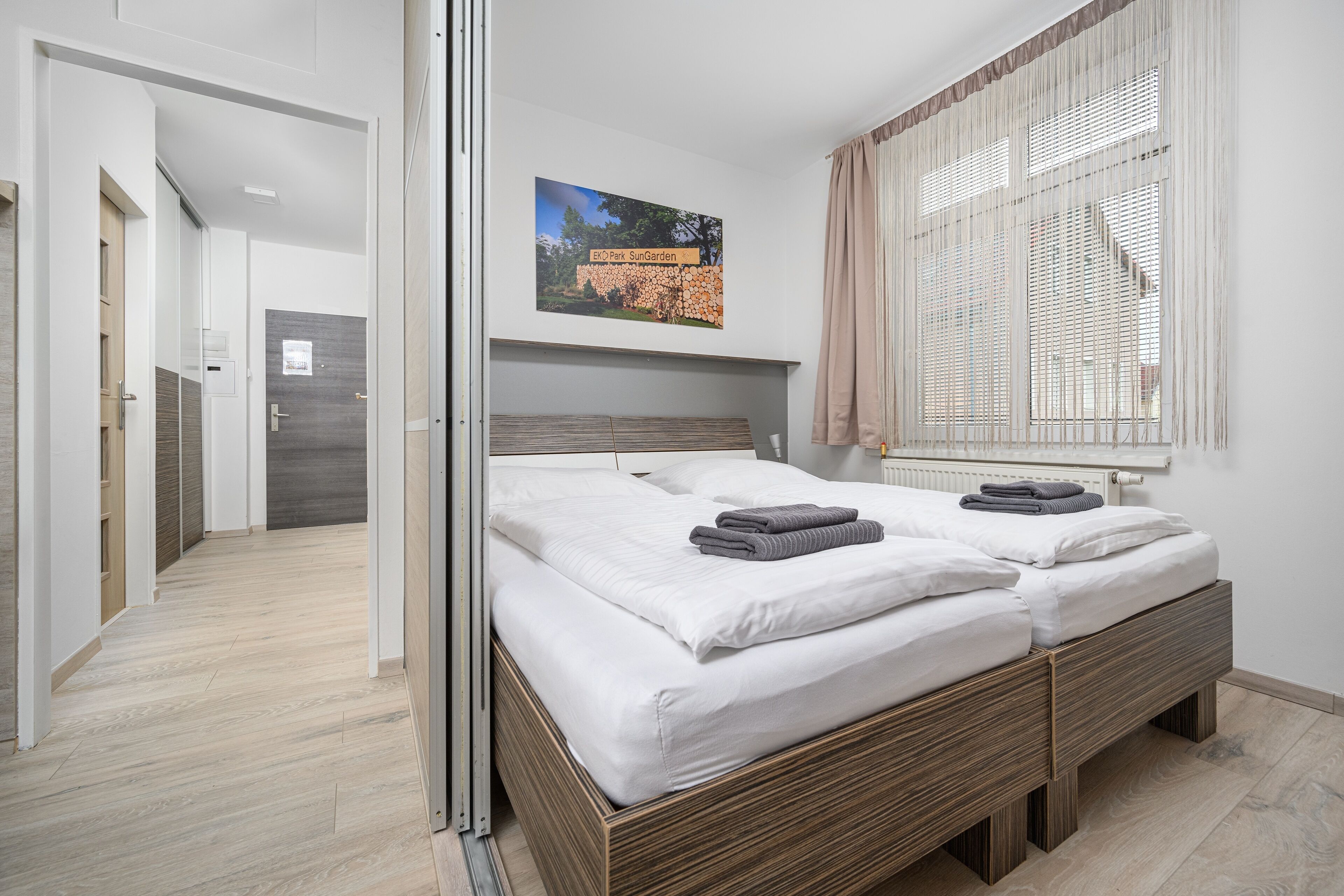 Een moderne hotelkamer met een groot bed, een houten hoofdbord, een raam met zonwering en een foto van een tuin aan de muur.