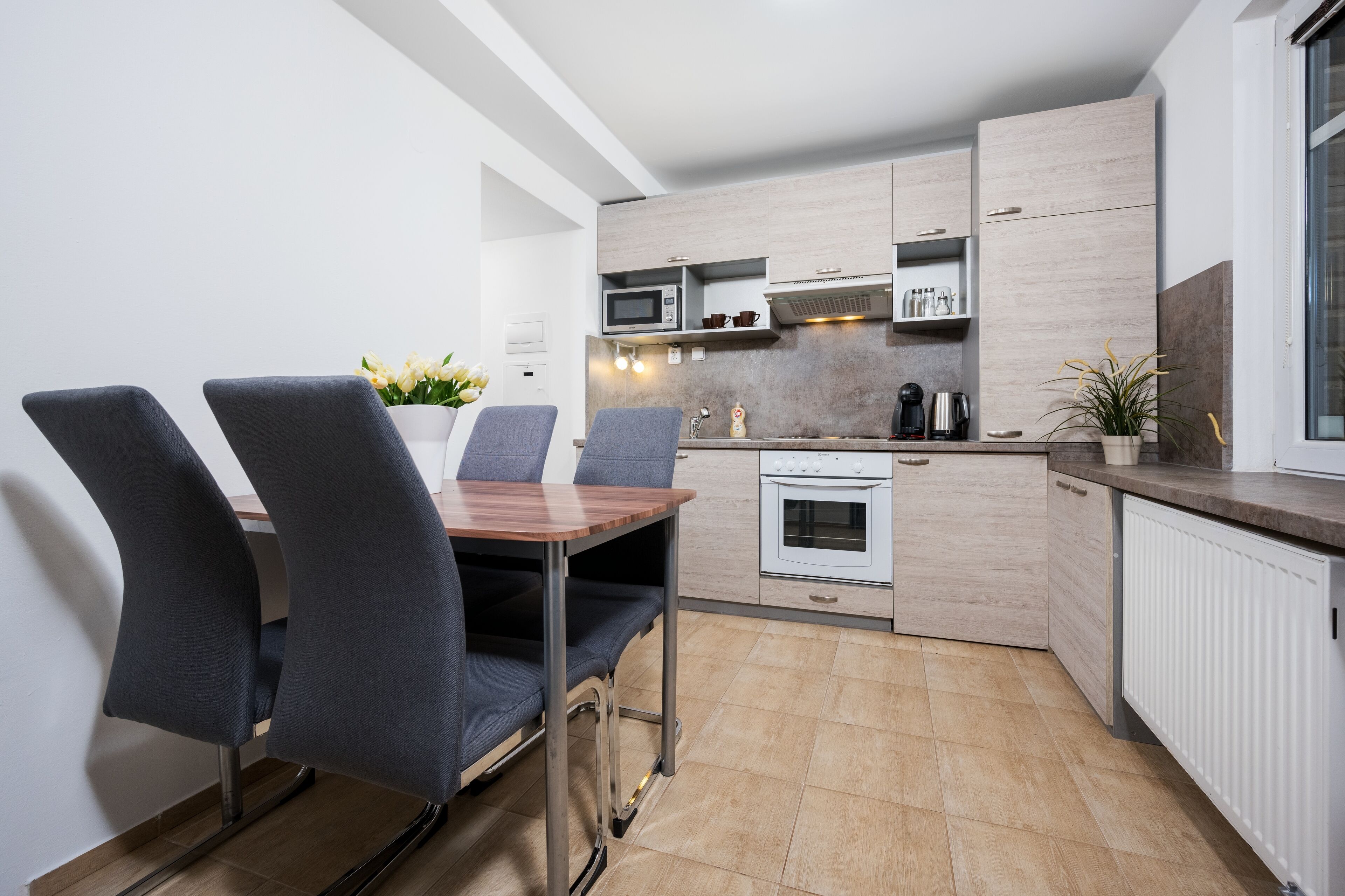 Cocina moderna con comedor, que incluye una mesa y sillas de madera, microondas, horno y una planta en maceta.