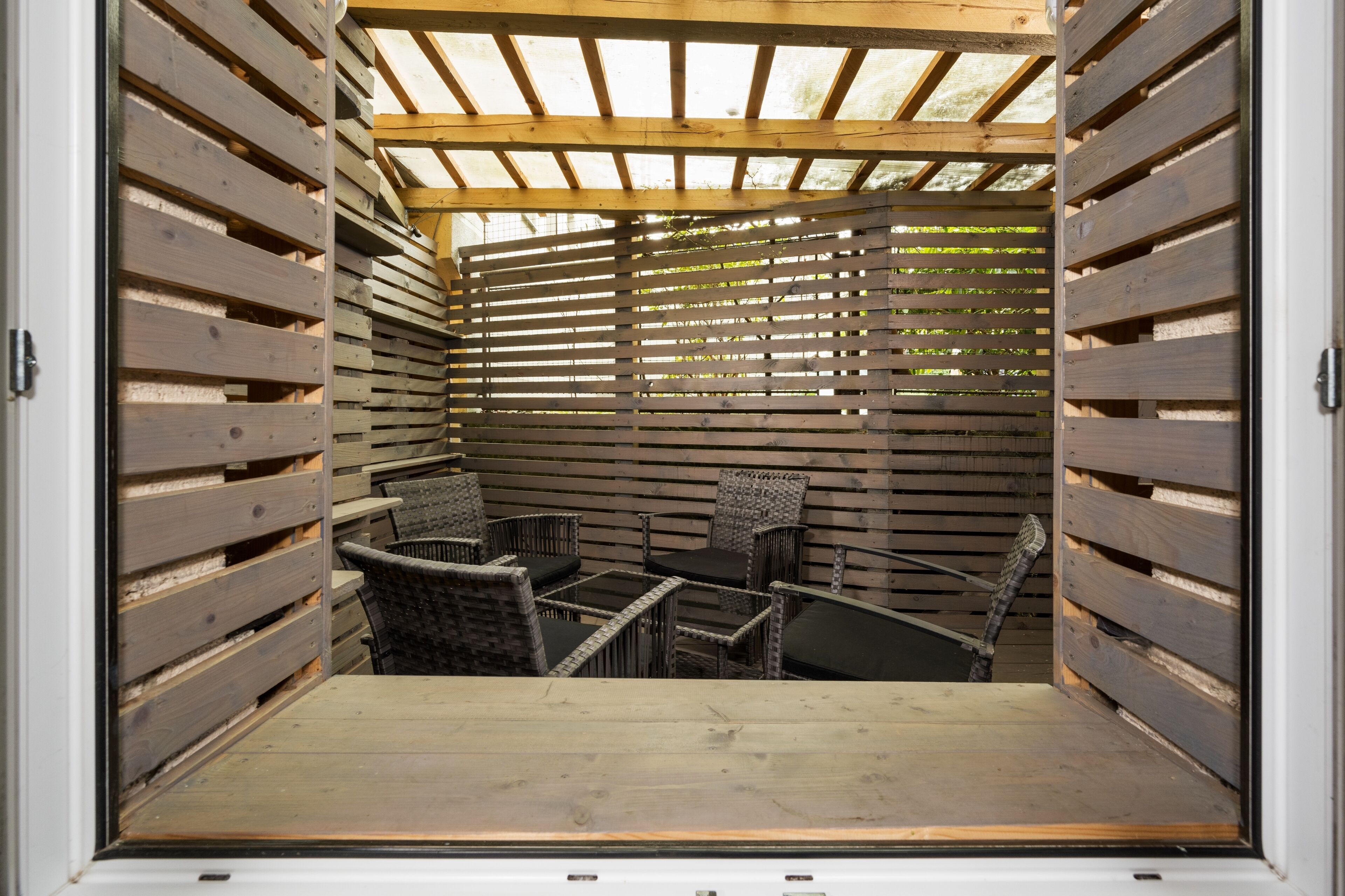 Un espacio de estar al aire libre cubierto con listones de madera, sillas de mimbre y una mesa.