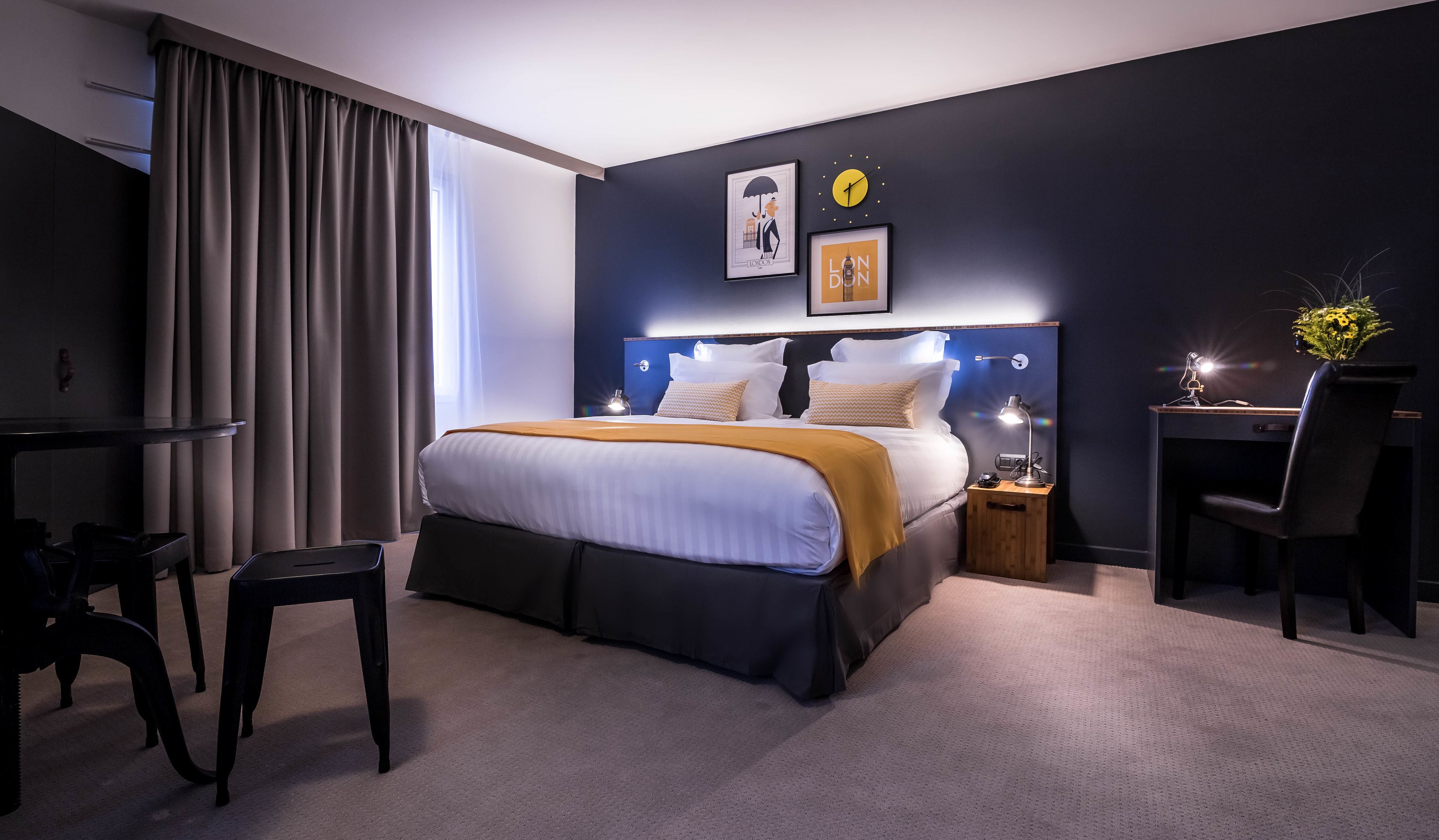 A modern hotel room with a large bed, bedside tables with lamps, a desk with a chair, and a view of the city.