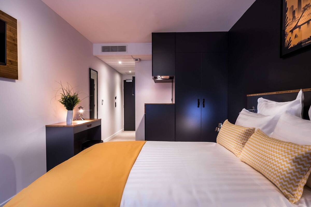A modern hotel room with a bed, bedside table, and a dark wardrobe.
