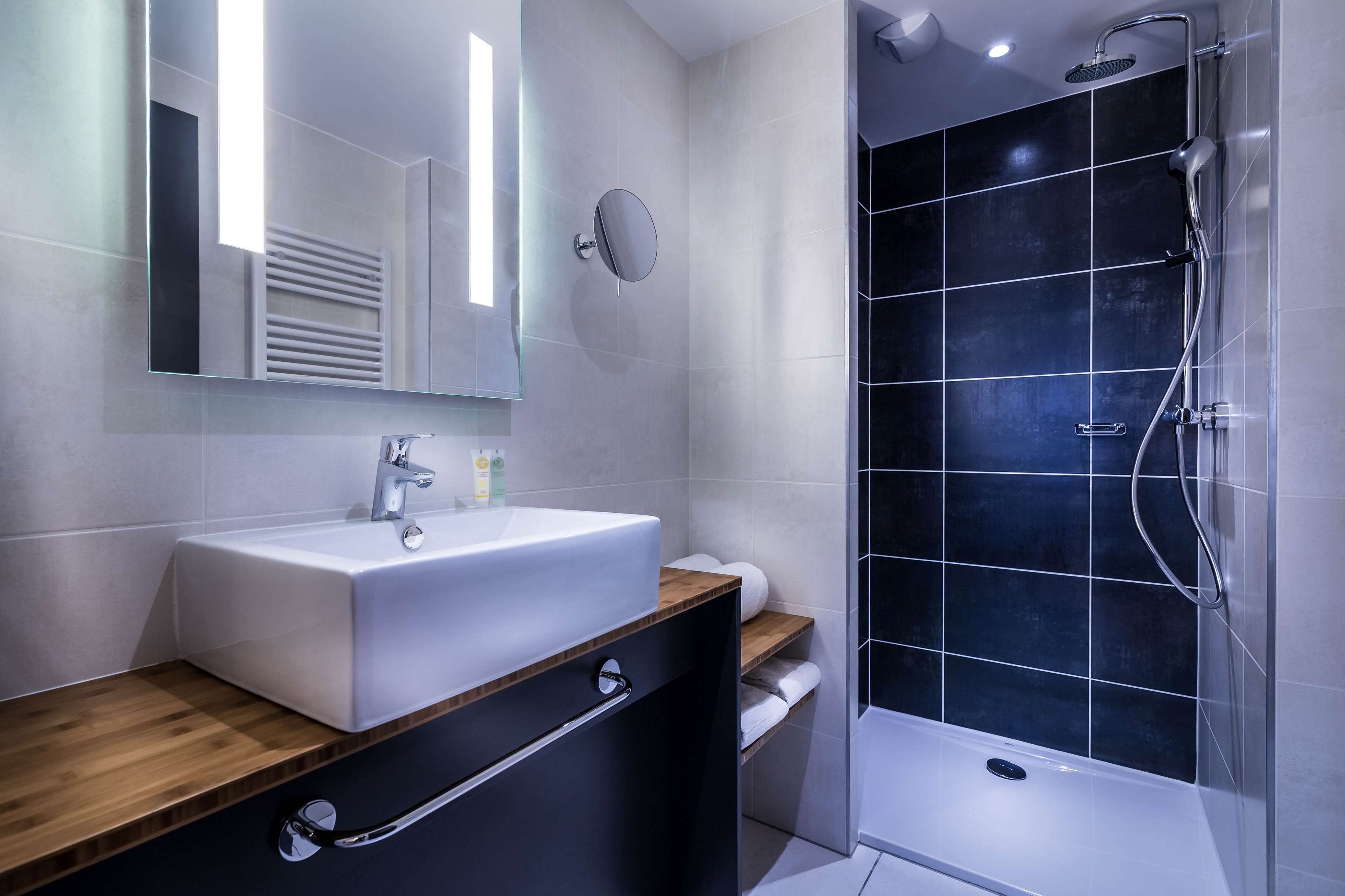 A modern bathroom with a white sink, a mirror, and a shower area with dark tiles.