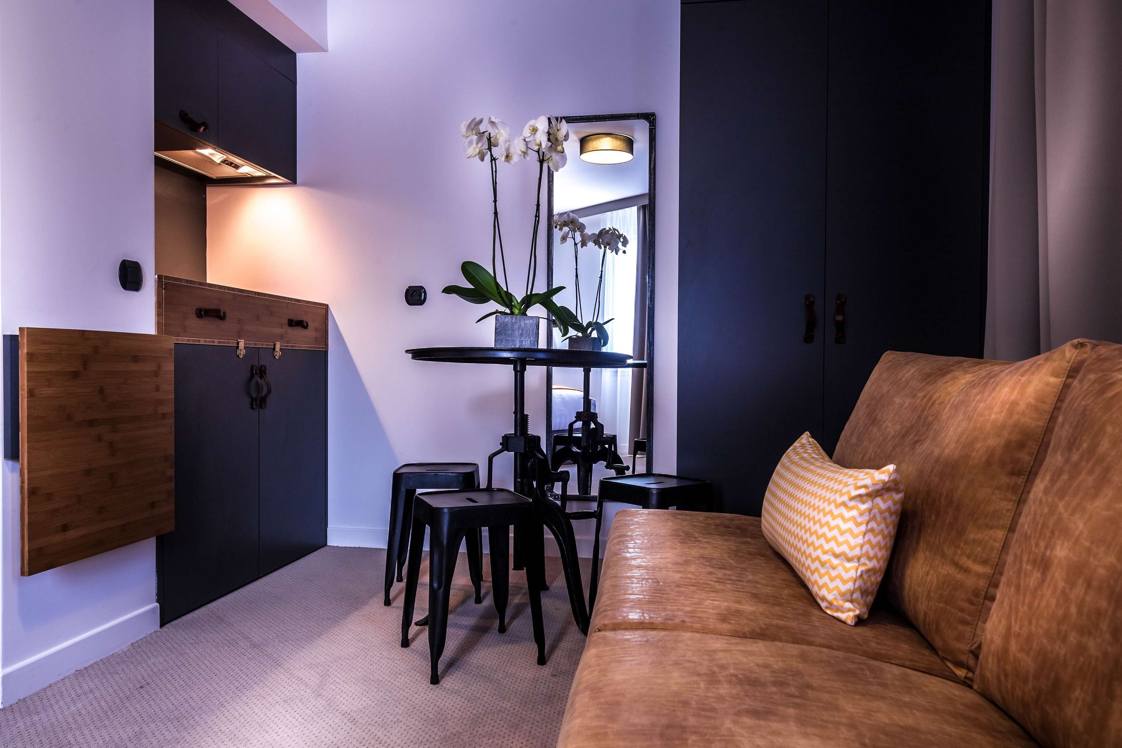 A modern living room with a brown sofa, a coffee table, and a black TV stand. There is a small table with a potted plant and a mirror above it.
