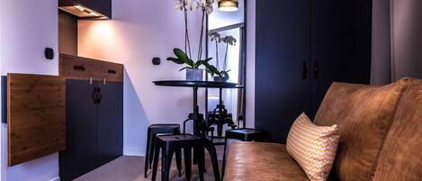 A modern living room with a brown sofa, a coffee table, and a black TV stand. There is a small table with a potted plant and a mirror above it.