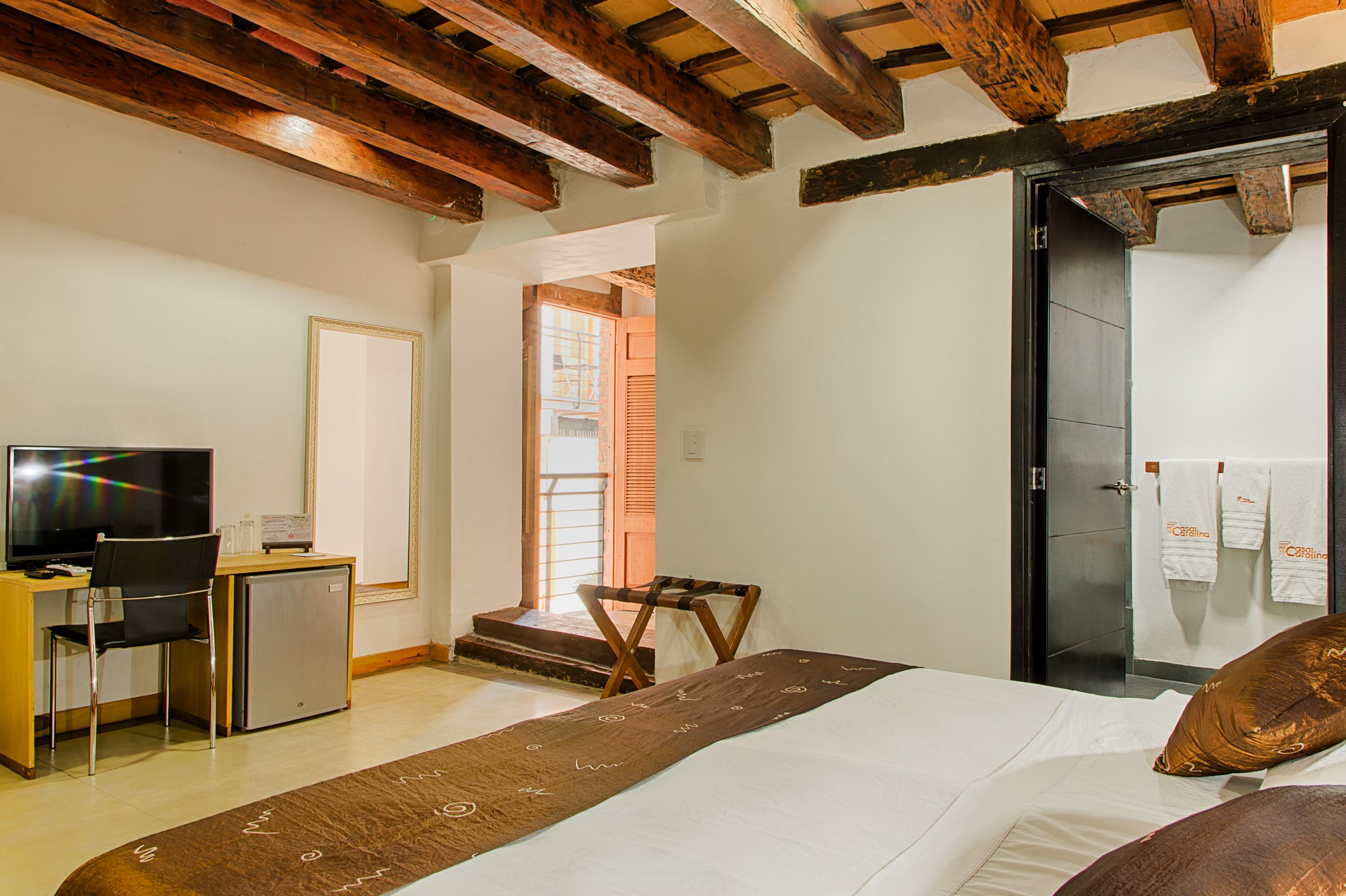 A hotel room with a bed, a desk with a television, a small refrigerator, and a chair.