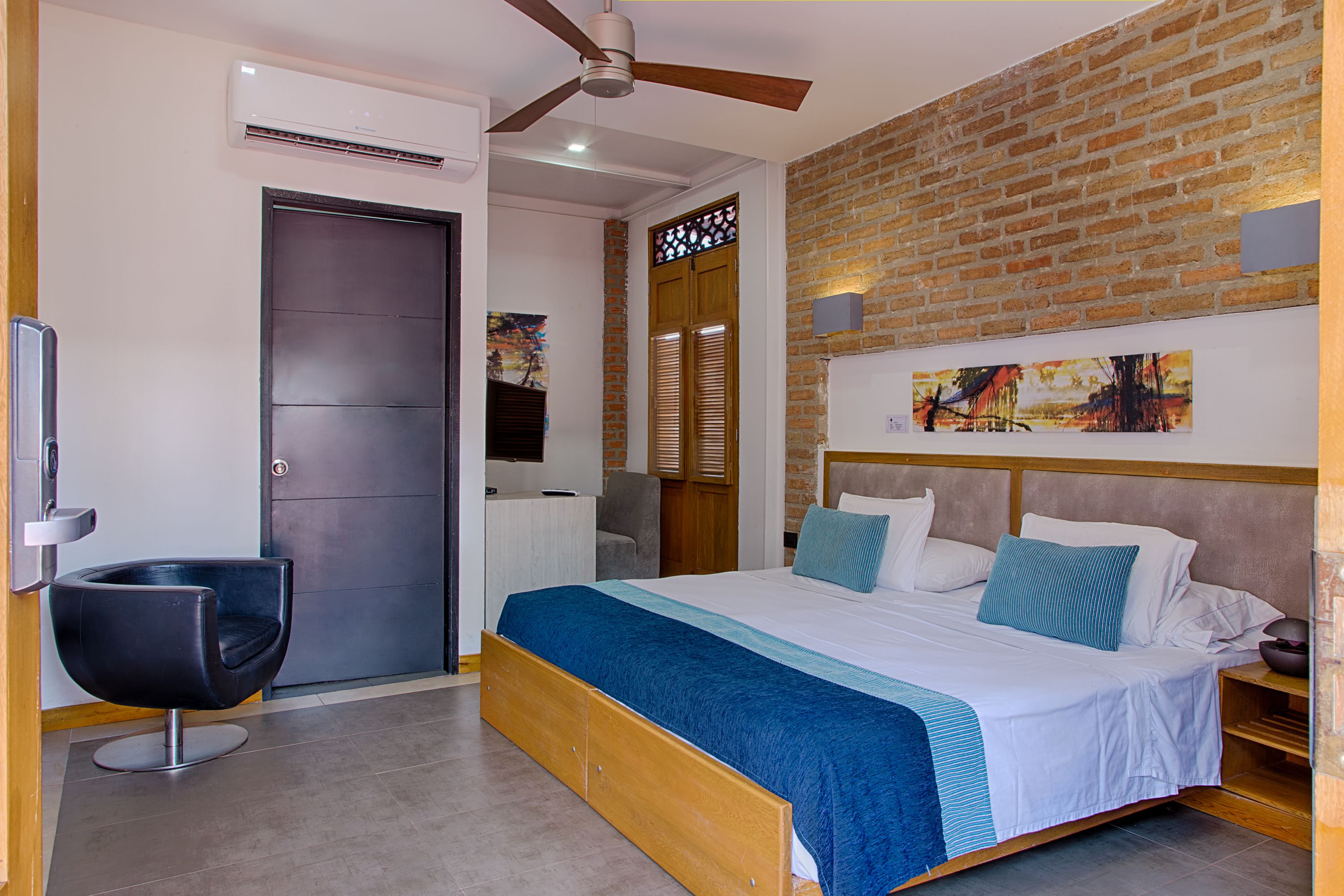 A modern bedroom with a large bed, a ceiling fan, a brick wall, and a door.