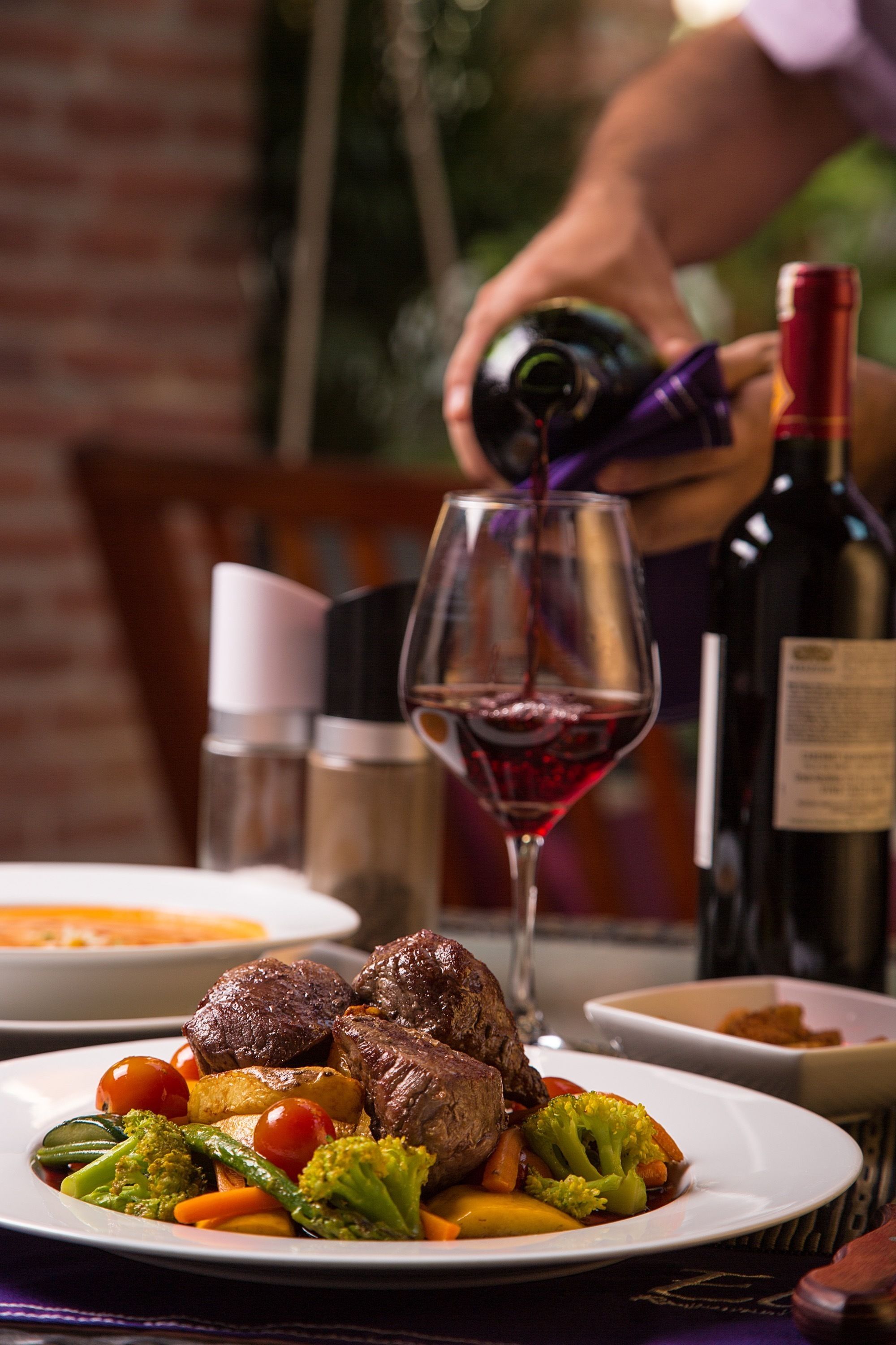 Une table à manger avec une assiette de nourriture, un verre de vin rouge et une bouteille de vin.