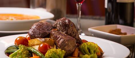 Une table à manger avec une assiette de nourriture, un verre de vin rouge et une bouteille de vin.