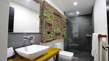 Un baño moderno con pared de piedra, un lavabo blanco, inodoro y mampara de ducha de vidrio.