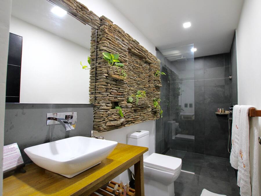 Een moderne badkamer met een stenen muur, een witte wasbak, een toilet en een douchecabine van glas.
