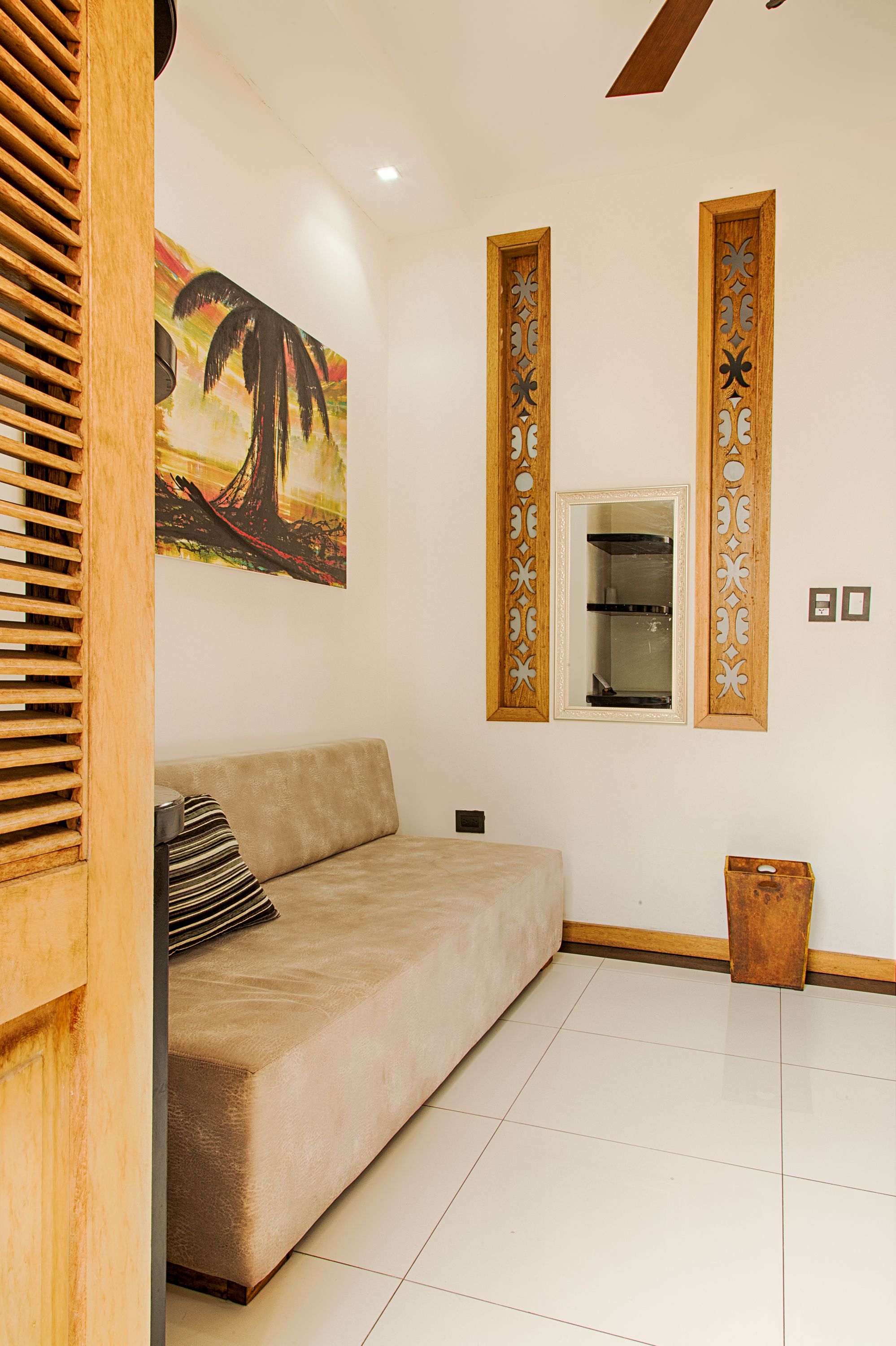 A living room with a beige sofa, a wooden sideboard, a painting, and a mirror with decorative wooden frames.