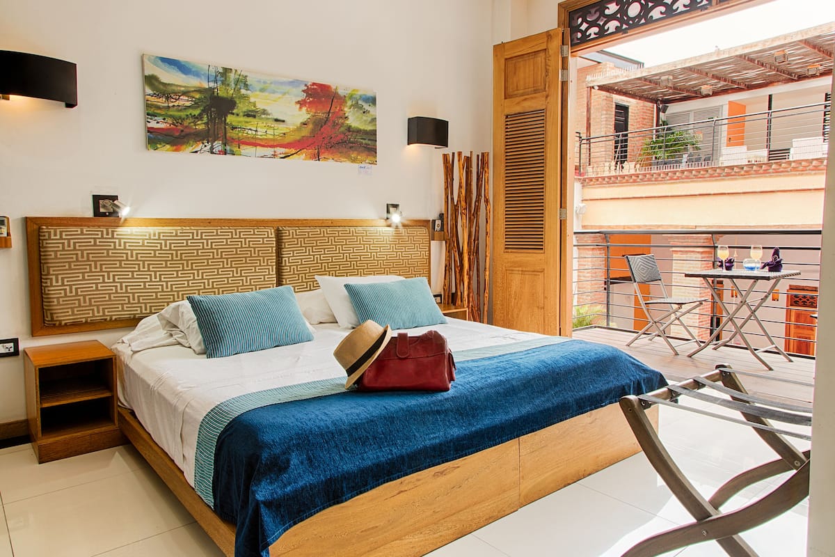 A bedroom with a bed, a nightstand, a painting, and a balcony with a table and chairs.