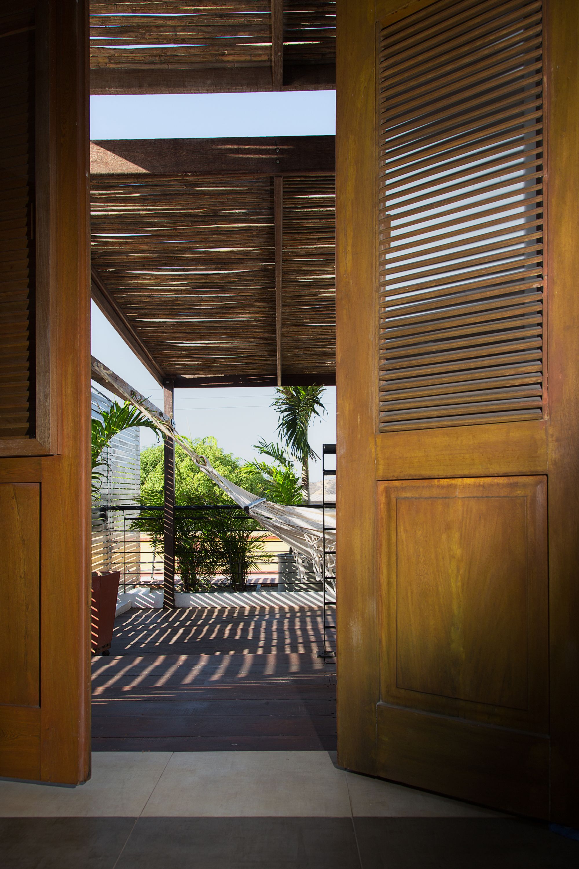 An interior space with a wooden door, a ceiling with horizontal slats, and a view of outdoor greenery.